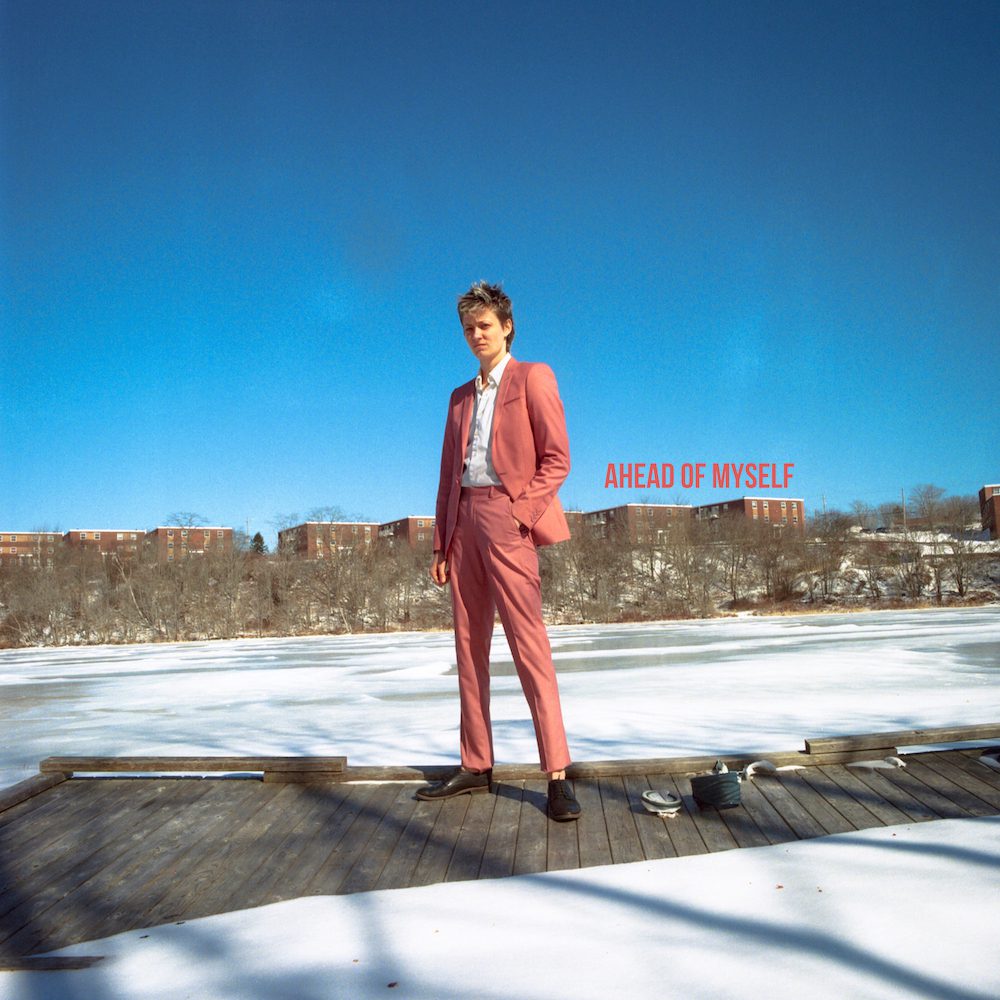 Mo Kenney press image of Mo in Nova Scotia standing on a wooden walkway wearing a peach trouser suit and white shirt looking confident for Ahead of Myself album promo